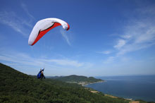 写真：山と海の見えるところをパラシュートが飛んでいる